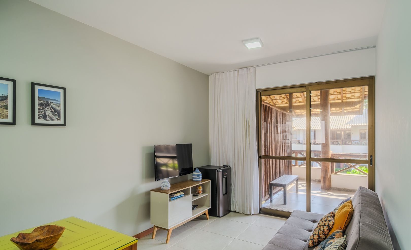 Una sala de estar con un sofá, un televisor, una mesita y un banco. Hay dos cuadros enmarcados en la pared.