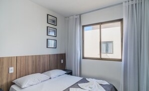 Ein Hotelzimmer mit einem Bett, einem Nachttisch, einem Fenster mit Vorhängen und drei gerahmten Bildern an der Wand.
