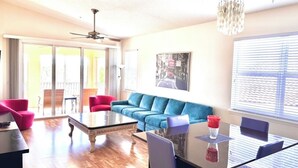 A spacious living area with a blue sofa, a glass coffee table, and a dining table with chairs.