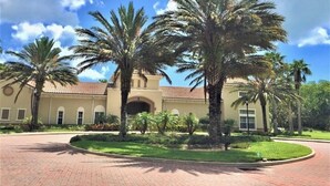 A building with a red-tiled roof, arched entrance, and palm trees in the foreground.