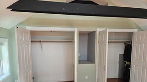 A room with a wooden floor, white closet doors, and a black beam on the ceiling. - Discreet 1 Bedroom getaway (Buffalo)