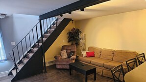 A living room with a staircase, a sofa, a chair, and a coffee table. - Discreet 1 Bedroom getaway (Buffalo)