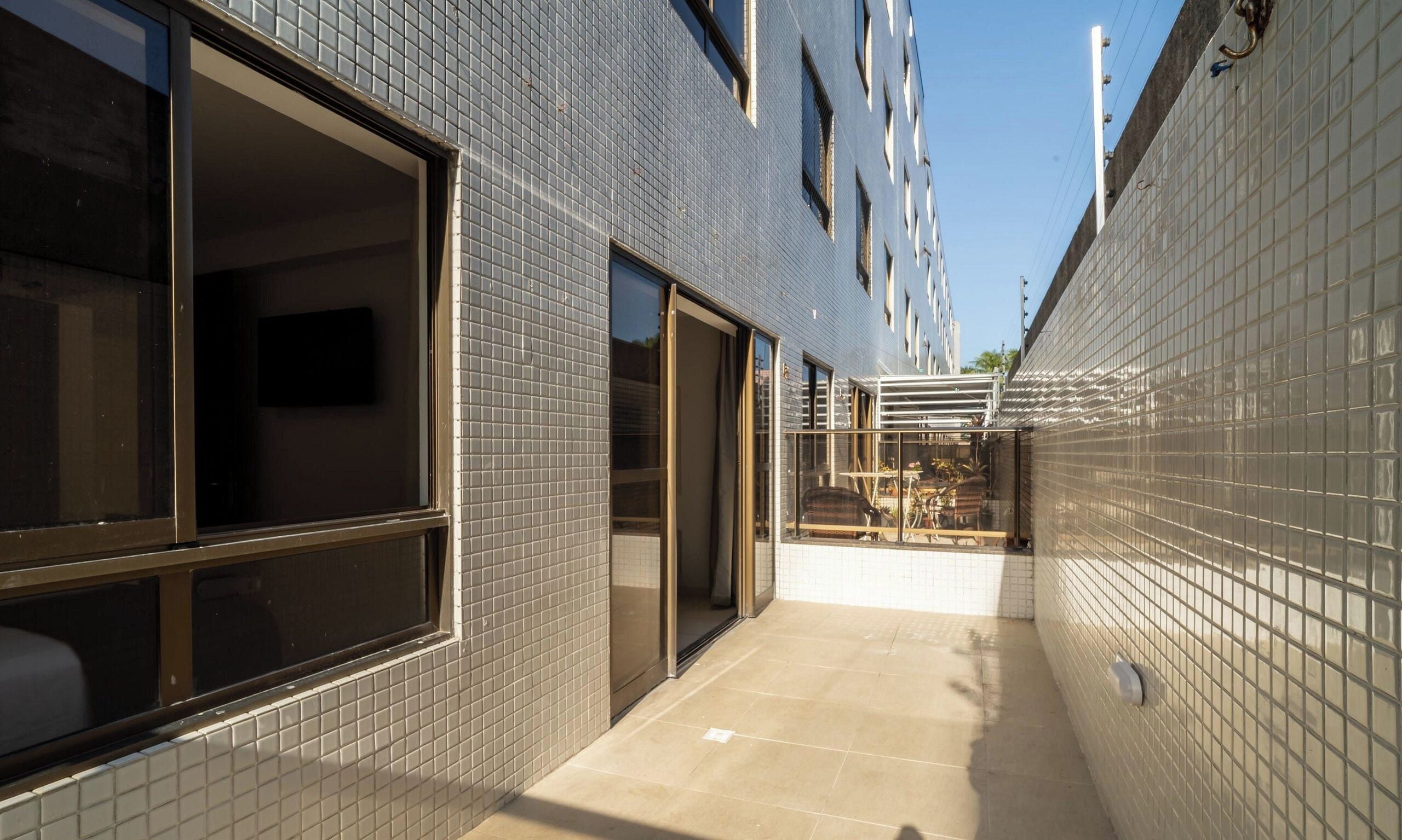 A narrow corridor with tiled walls and a tiled floor, leading to a building entrance with a glass door.
