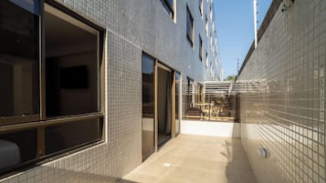 A narrow corridor with tiled walls and a tiled floor, leading to a building entrance with a glass door.