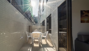Un patio exterior estrecho con una mesa, sillas, un vidrio y una pared de azulejos.