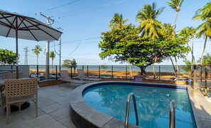 Zona de piscina con sillas de descanso, una sombrilla grande y vista a la playa y al océano.