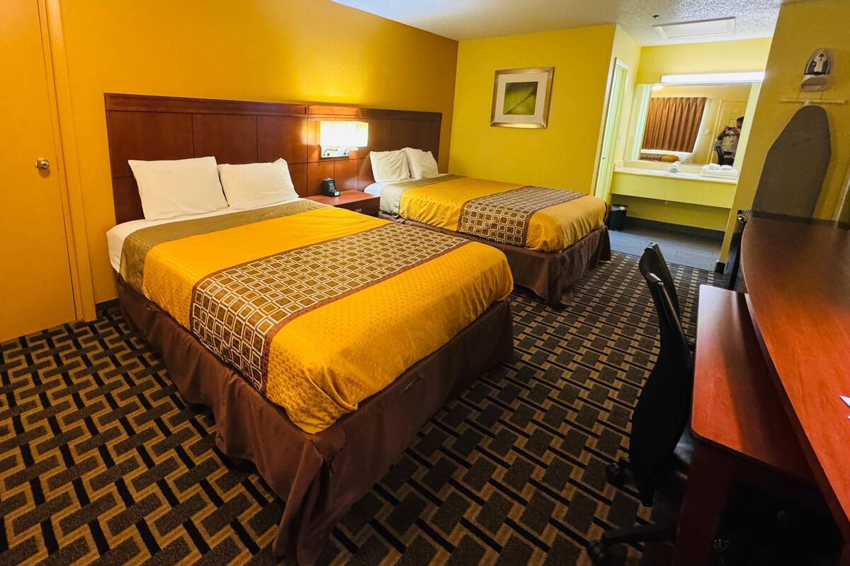 A hotel room with two beds, a desk, a chair, a nightstand, a lamp, and a mirror.