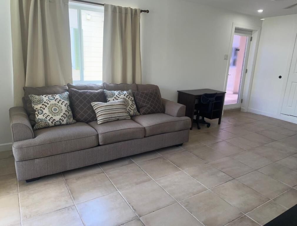 A living room with a beige sofa, patterned cushions, a small black table, and a door in the background.