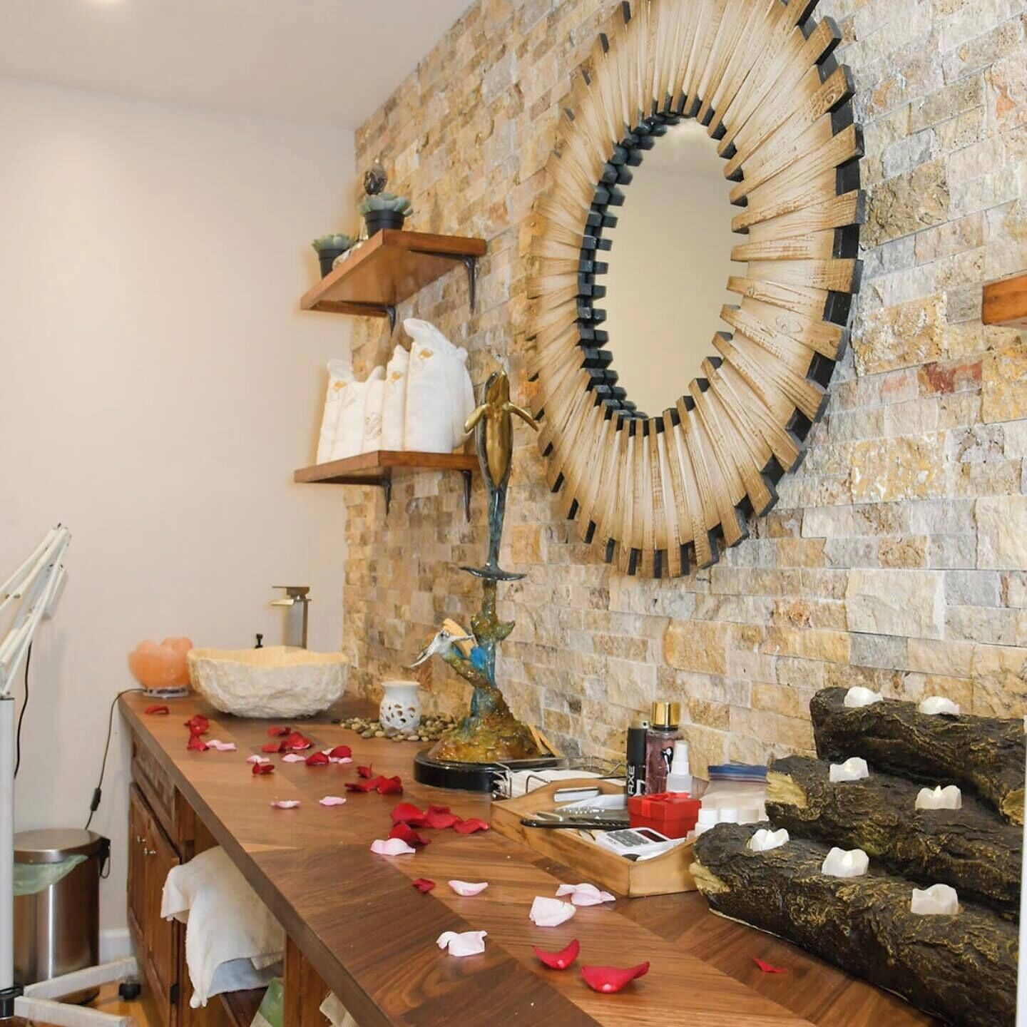 A bathroom with a stone wall, a wooden vanity, a large mirror, and a decorative fountain.