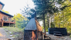 A metal fire pit with a chimney, surrounded by trees and a wooden deck.