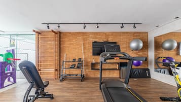 Un gimnasio en casa con cinta de correr, banco de pesas y diverso equipo de ejercicio.