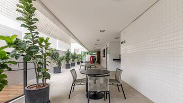 Un espacio interior moderno con un largo pasillo, plantas en macetas, una mesa redonda con sillas y una zona de juegos al fondo.