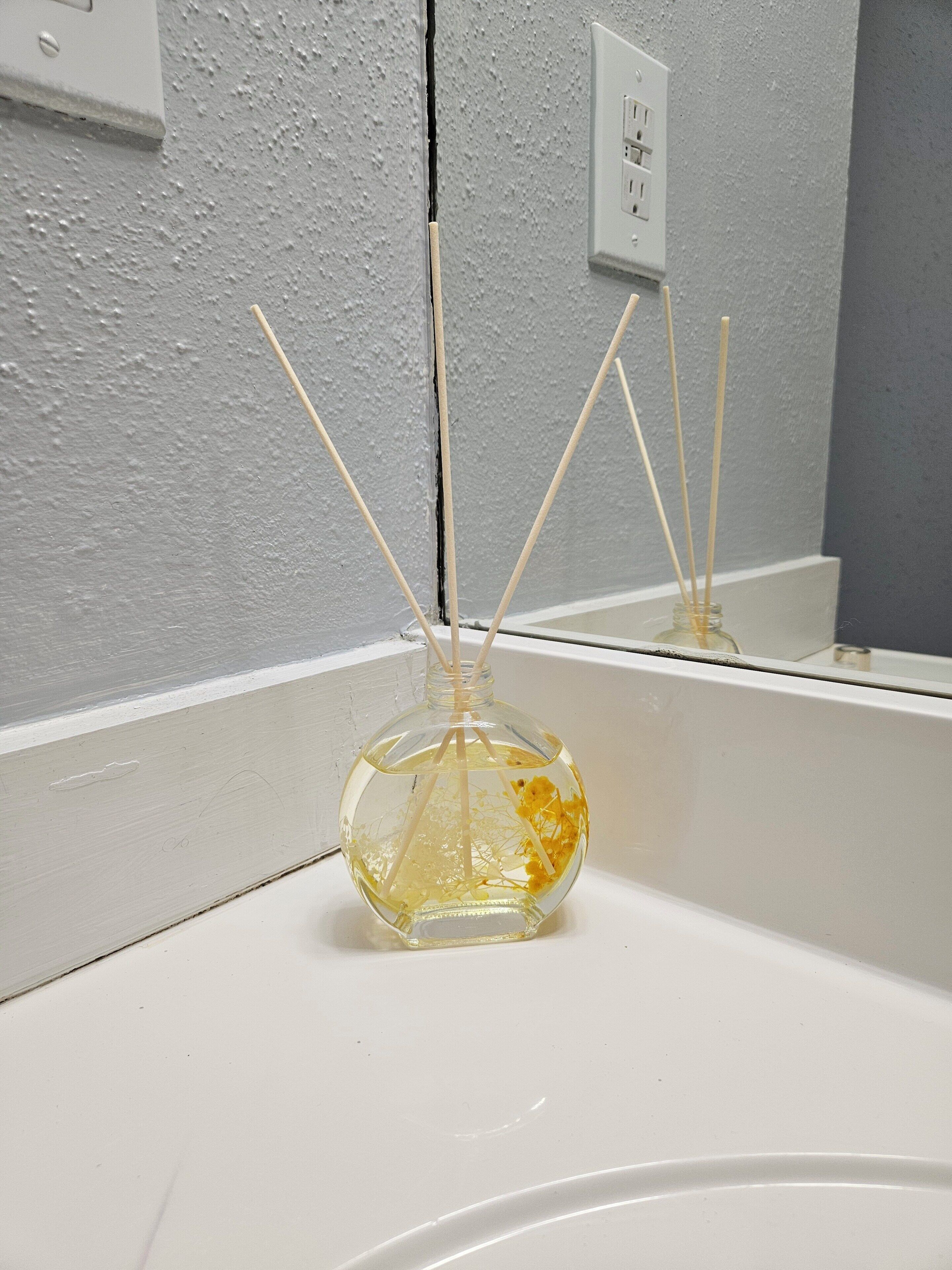 A bathroom sink with a glass bottle containing a yellow liquid and reed sticks.