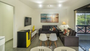 Un salon moderne comprenant un canapé, deux fauteuils, une table basse, un téléviseur et des œuvres d’art accrochées au mur.