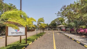 Un chemin pavé mène à un bâtiment sur lequel est apposée une enseigne indiquant « clubhouse de Genipabu ».