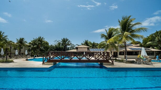 Une piscine avec une terrasse en bois et des palmiers en arrière-plan.