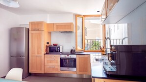 A compact kitchen with wooden cabinets, a built-in oven, a microwave, and a sink. - Apartment 100m from the beach - historic center (Collioure)