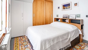 A bedroom with a bed, a wardrobe, a shelf with books, and a patterned floor. - Apartment 100m from the beach - historic center (Collioure)