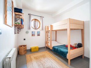 A room with a bunk bed, a small shelf with books, a round mirror, and a woven basket. - Apartment 100m from the beach - historic center (Collioure)