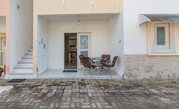 A building with a white exterior, a set of stairs leading to a door, and a patio area with a table and chairs.