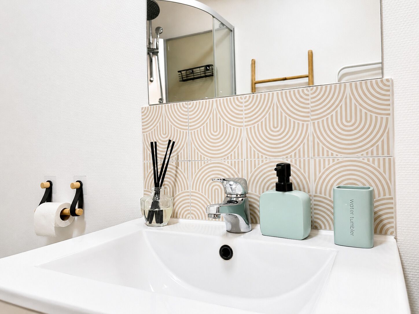 A bathroom with a white sink, a mirror, a shower, and a patterned wall.
