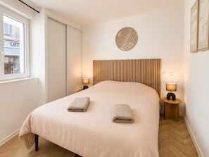 A hotel room with a large bed, two bedside lamps, a window with a view of a building labeled 'LOT,' and a decorative wall piece above the bed.