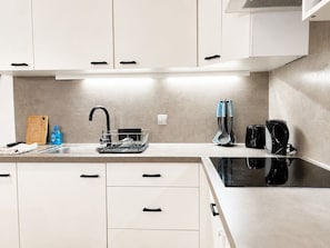 A modern kitchen with white cabinets, a black faucet, a dish rack, a cutting board, a bottle of dish soap, a coffee maker, and a kettle.
