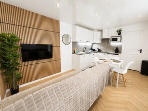 Una cocina moderna con armarios blancos, un televisor de pantalla plana y un comedor con una mesa para dos.