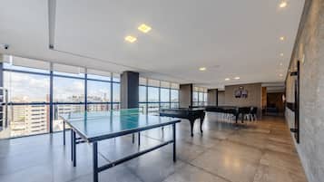 A spacious indoor area with a ping pong table, a piano, and large windows offering a city view.