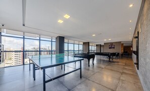 A spacious indoor area with a ping pong table, a piano, and large windows offering a city view. - Studio w/ Pool 300m From the Beach- Maceio Eti0724 (Maceió)