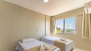 A hotel room with two beds, a large window with a view of buildings, and an air conditioning unit. - Apartments 450m From the Beach in Ilheus - ERN (Ilhéus)