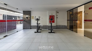 A gym with two stationary bikes, a red door, and a tiled floor. - Cozy Studio 376m From the Beach - Ere418 (Maceió)