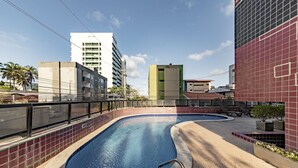 A swimming pool with a curved design, surrounded by a tiled walkway and a metal fence. - Cozy Studio 376m From the Beach - Ere418 (Maceió)