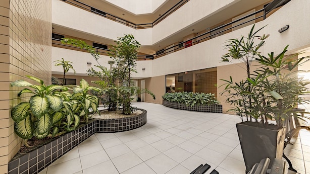 A spacious indoor atrium with multiple levels, featuring tiled floors, potted plants, and a central seating area. - Cozy Studio 376m From the Beach - Ere418 (Maceió)