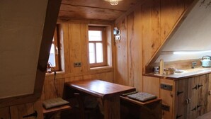 A wooden cabin with a dining table, benches, and a kitchenette. - Bohlenstube guest apartment (Birkenfelde)