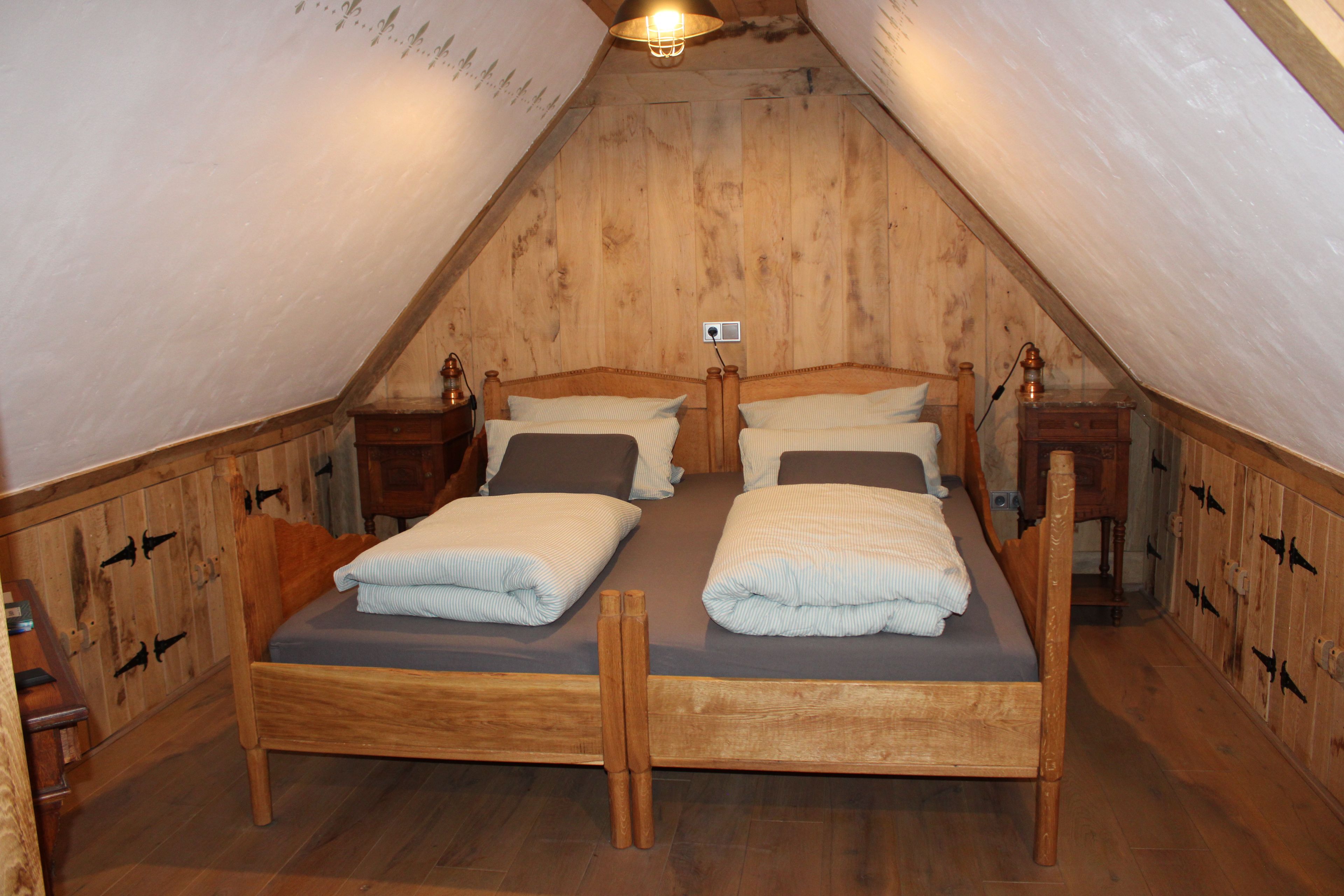 A room with two wooden beds, a wooden ceiling, and a small table with a lamp.