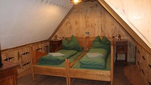A small, cozy attic bedroom with a sloped ceiling, wooden walls, and two single beds with green bedding. - Bohlenstube guest apartment (Birkenfelde)