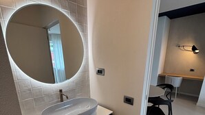 Casa de banho moderna com um espelho oval grande, lavatório suspenso, armários escuros e chão em tons claros.