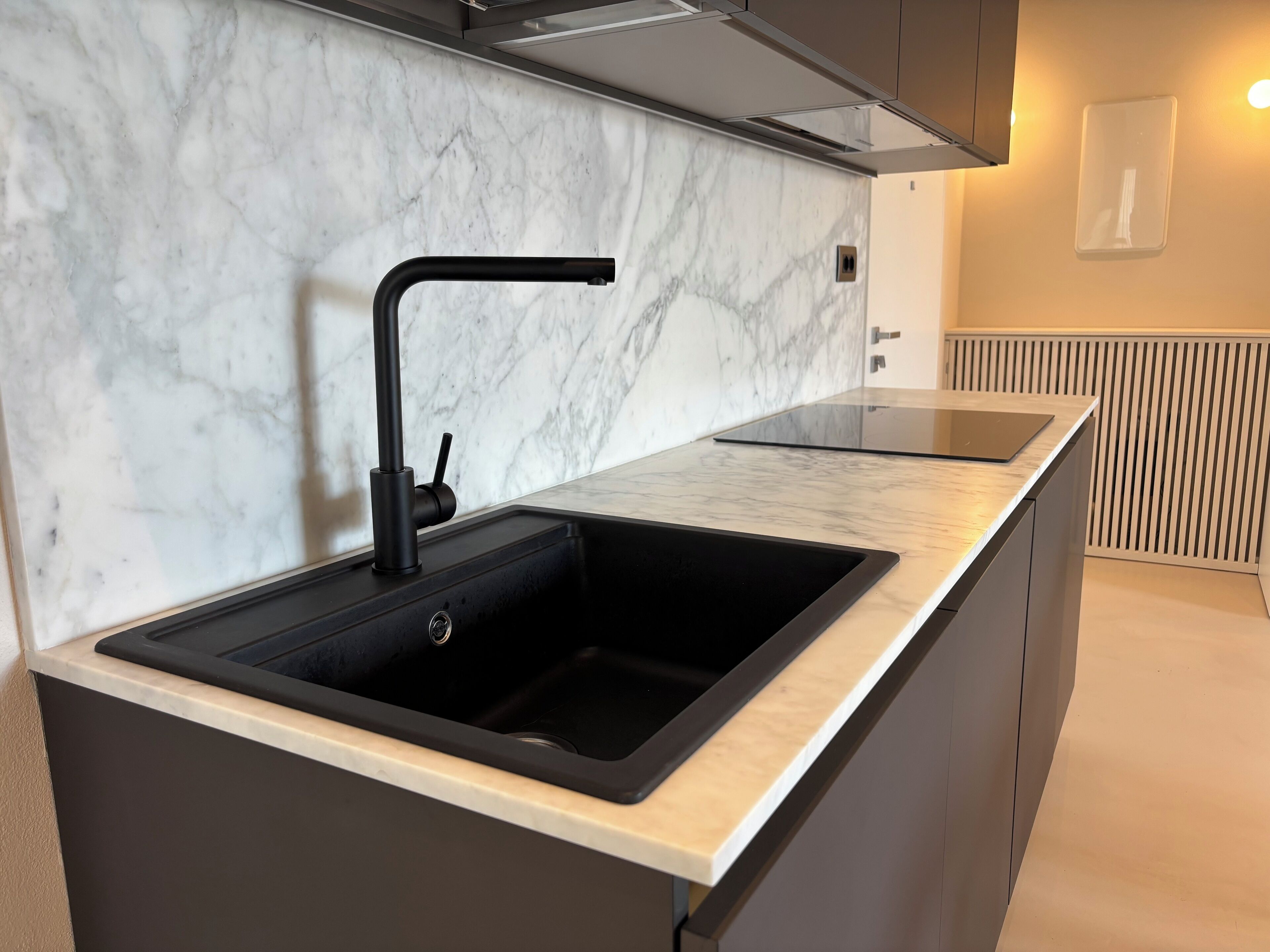 Una cocina moderna con un lavamanos negro, salpicadero de mármol y una estufa empotrada.