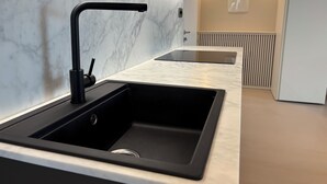 Uma cozinha moderna com pia preta, painel de mármore branco e fogão embutido.