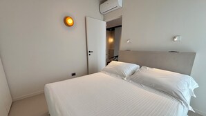 Quarto de hotel com cama, porta, ar condicionado e luminária.