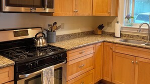 Cocina con gabinetes de madera, electrodomésticos de acero inoxidable, encimeras de granito y una ventana con vistas.