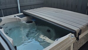 Un jacuzzi con cubierta de madera, rodeado por una cerca de madera y un muro de piedra.