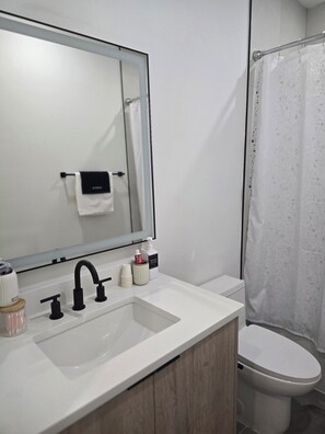 Ein Badezimmer mit weißem Waschbecken, einem Spiegel, einer Toilette und einer Duschvorhang.