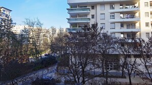 En flervåningsbyggnad med bostäder, balkonger, en parkeringsplats och träd i förgrunden.