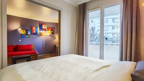 Ett hotellrum med en stor säng, en röd soffa, ett litet bord och en vägg prydd med färgstarka konstverk.