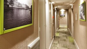 En hotellkorridor med svartvita fotografier i ramar på väggarna, ett heltäckningsmatta på golvet och ett element.
