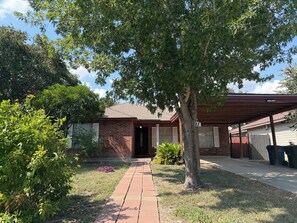 A brick building with a covered porch, a pathway leading to the entrance, and a tree in the foreground.