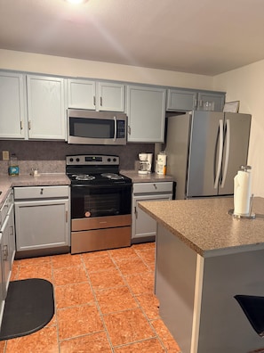 A kitchen with grey cabinets, a stainless steel refrigerator, a microwave, an oven, and a coffee maker.