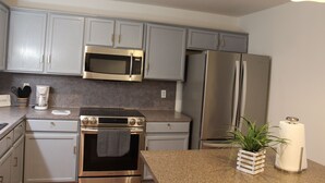 A modern kitchen with stainless steel appliances, light grey cabinets, and a granite countertop.